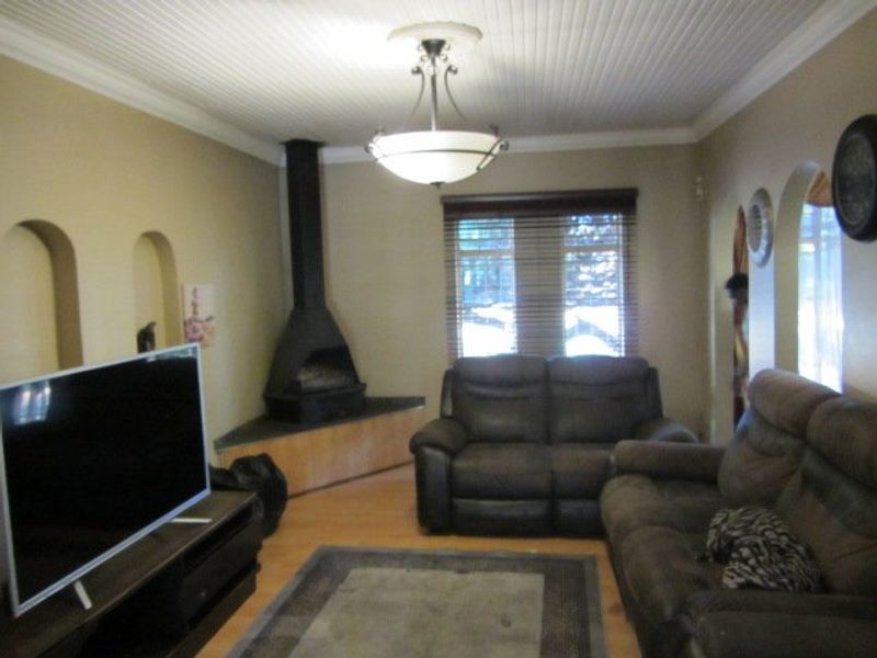 A cozy living room featuring a corner fireplace, unique arched wall niches, beadboard ceiling detailing, and laminate flooring.