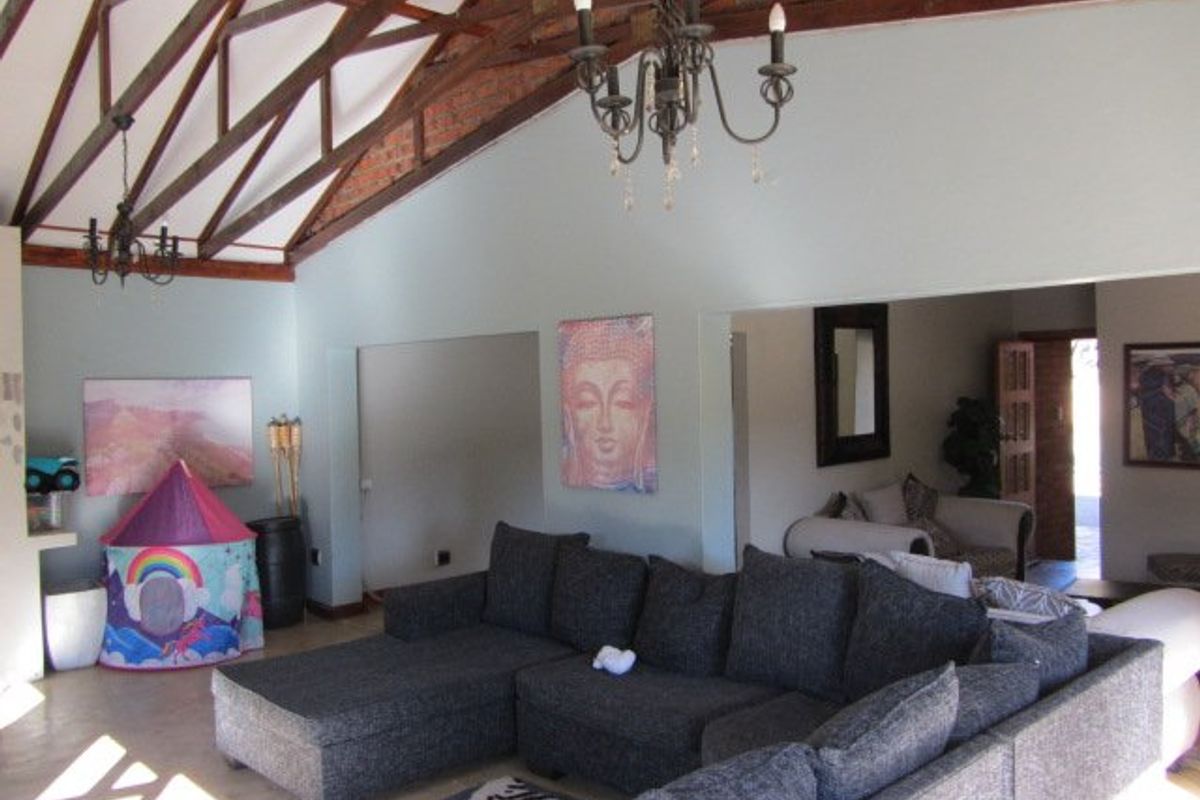 Spacious living area featuring a high vaulted ceiling with exposed timber trusses, brick accents, and a classic wrought iron chandelier.