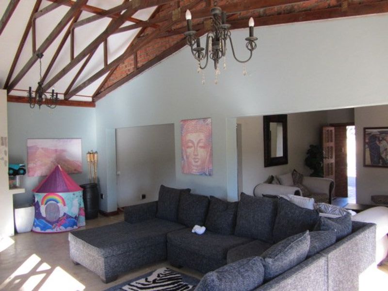 Spacious living area featuring a high vaulted ceiling with exposed timber trusses, brick accents, and a classic wrought iron chandelier.