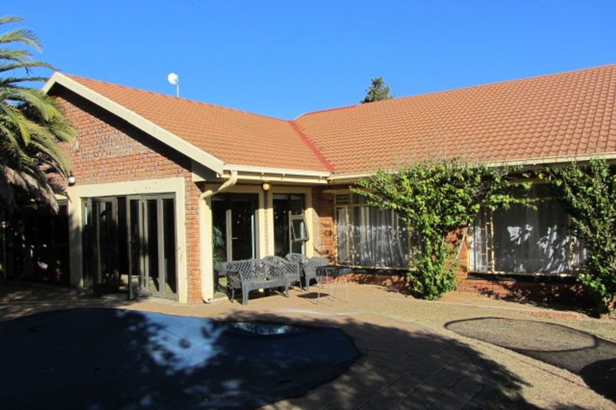 Rear view of the property featuring a brick facade, tiled roof, paved patio area, and a swimming pool with a cover.