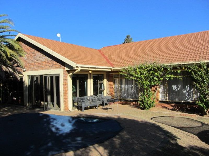 Rear view of the property featuring a brick facade, tiled roof, paved patio area, and a swimming pool with a cover.