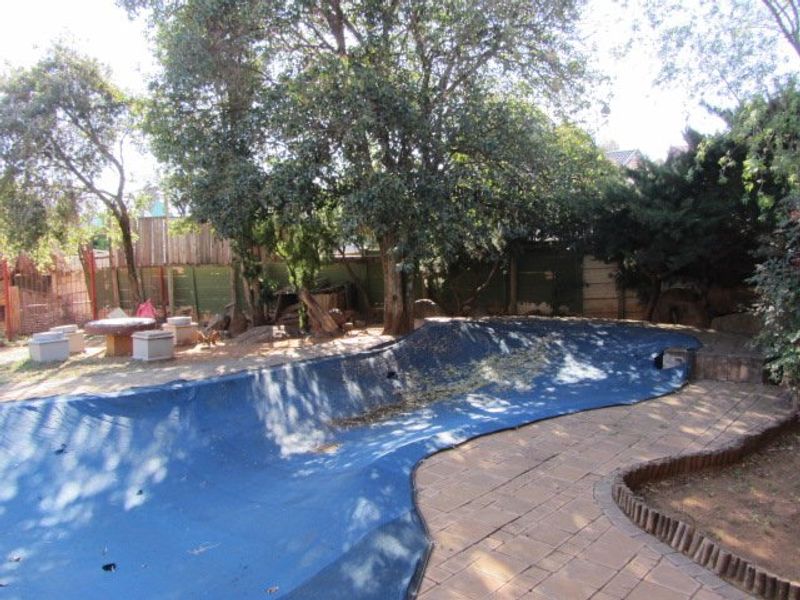 Outdoor pool area featuring a paved patio surround, perimeter fencing, and a large swimming pool covered with a protective safety cover.