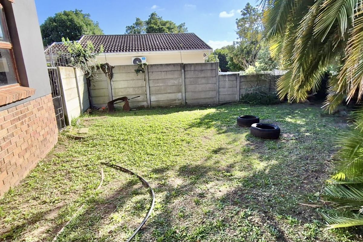 A rear garden area featuring a brick facade, precast concrete boundary wall, and established palm tree, requiring landscaping and maintenance.