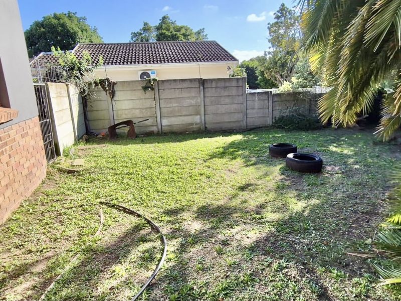 A rear garden area featuring a brick facade, precast concrete boundary wall, and established palm tree, requiring landscaping and maintenance.