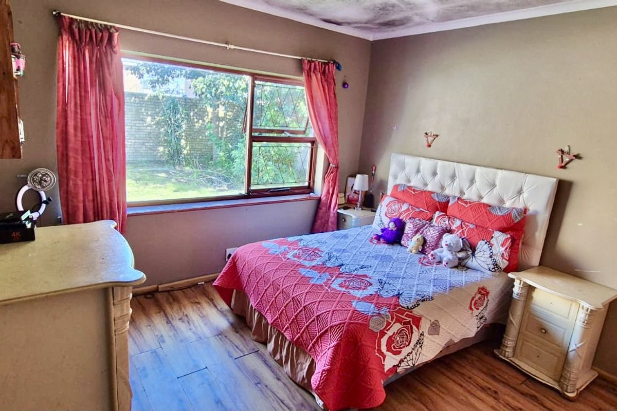 A bedroom featuring laminate flooring and a large window, currently showing signs of ceiling water damage and dated wall finishes.