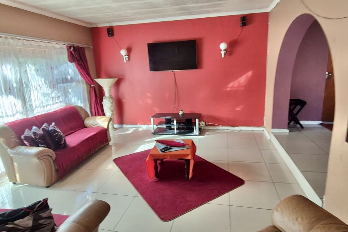 A living room featuring tiled flooring, an arched entryway, and wall-mounted lighting, currently requiring cosmetic updates to the ceiling and wall finishes.