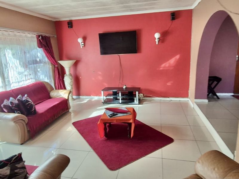 A living room featuring tiled flooring, an arched entryway, and wall-mounted lighting, currently requiring cosmetic updates to the ceiling and wall finishes.