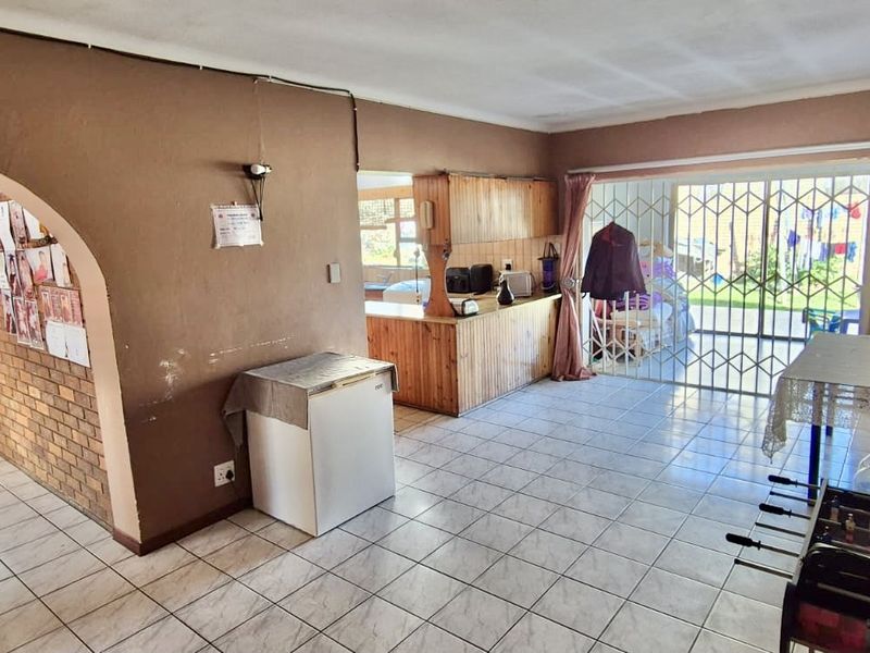 Open-plan living and kitchen area featuring tiled flooring, a brick archway, and wooden cabinetry, with direct access to the exterior through a security gate.