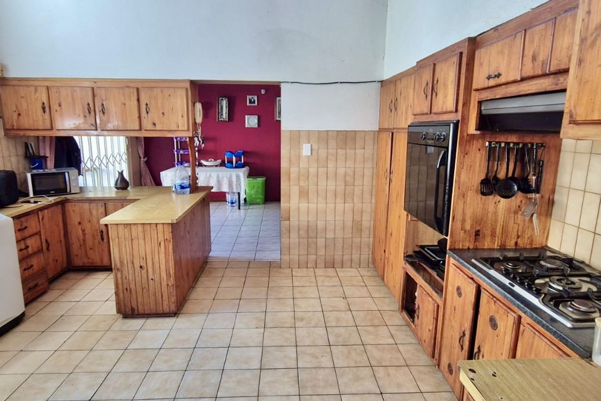 A functional kitchen featuring extensive wooden cabinetry, built-in oven, gas hob, and tiled finishes, offering a traditional layout with a breakfast counter.