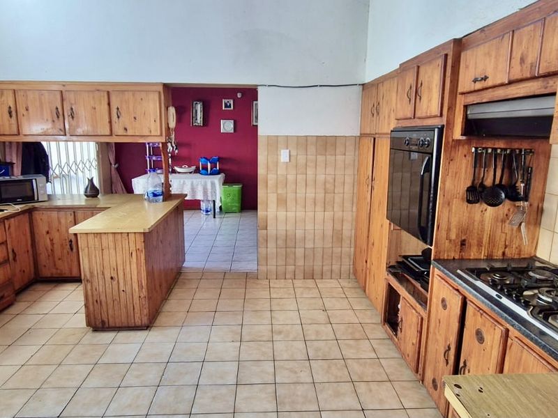 A functional kitchen featuring extensive wooden cabinetry, built-in oven, gas hob, and tiled finishes, offering a traditional layout with a breakfast counter.