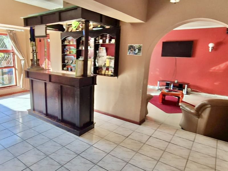 A dedicated bar area featuring a built-in wooden counter and shelving, leading through an archway into an adjacent living space with tiled flooring.