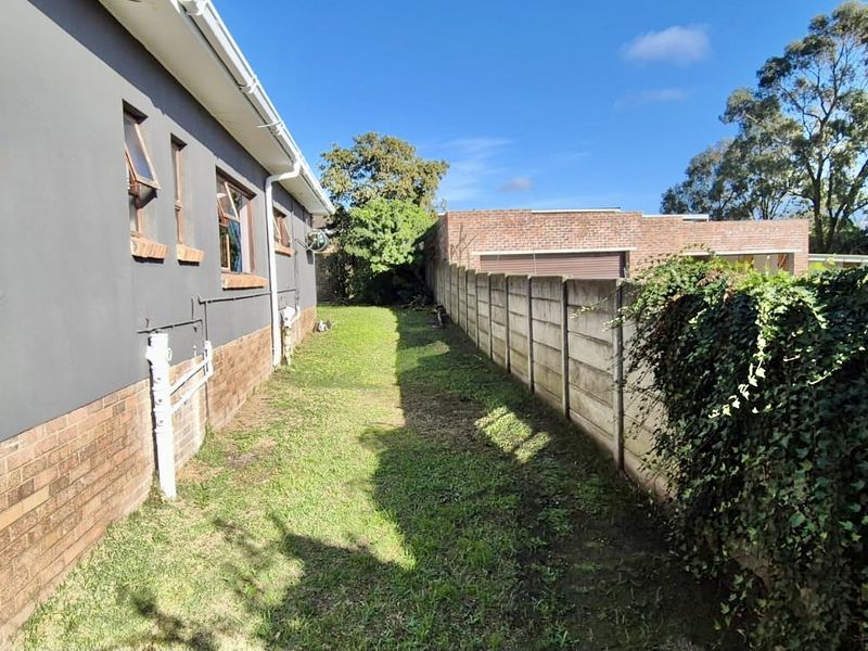 A side view of the property showing a narrow garden strip, brick boundary wall, and the exterior facade with casement windows.