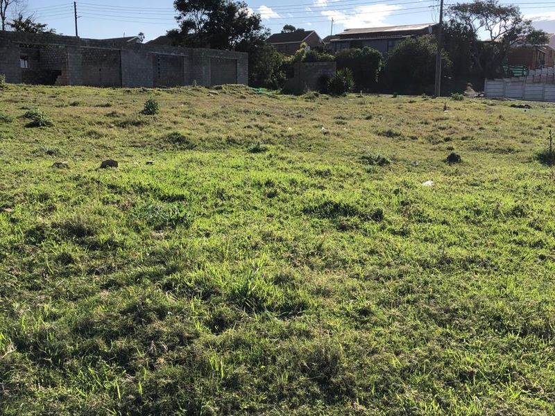 A view of a vacant residential plot featuring grass coverage and surrounding neighborhood infrastructure.