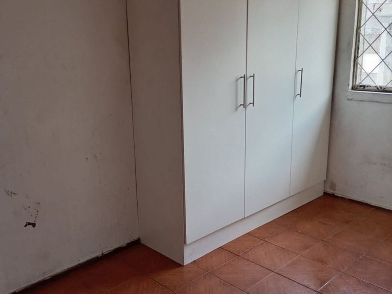 A bedroom featuring tiled flooring, a built-in wardrobe, and a timber ceiling, currently requiring cosmetic updates to the wall finishes and skirting.