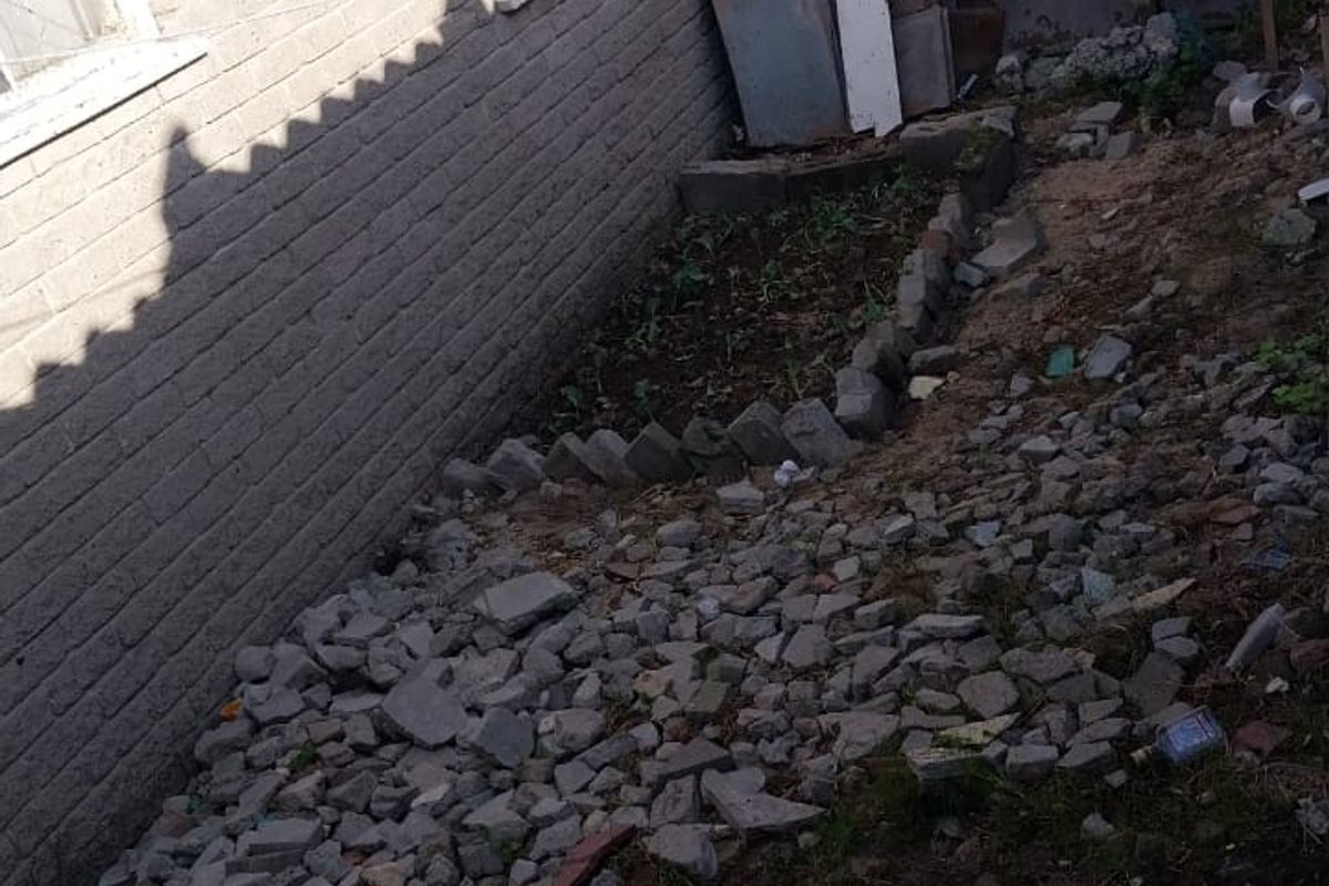 Rear exterior area showing brick building facade, guttering, and a yard space currently covered in construction debris and rubble.