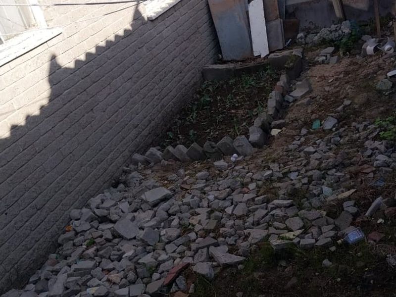 Rear exterior area showing brick building facade, guttering, and a yard space currently covered in construction debris and rubble.