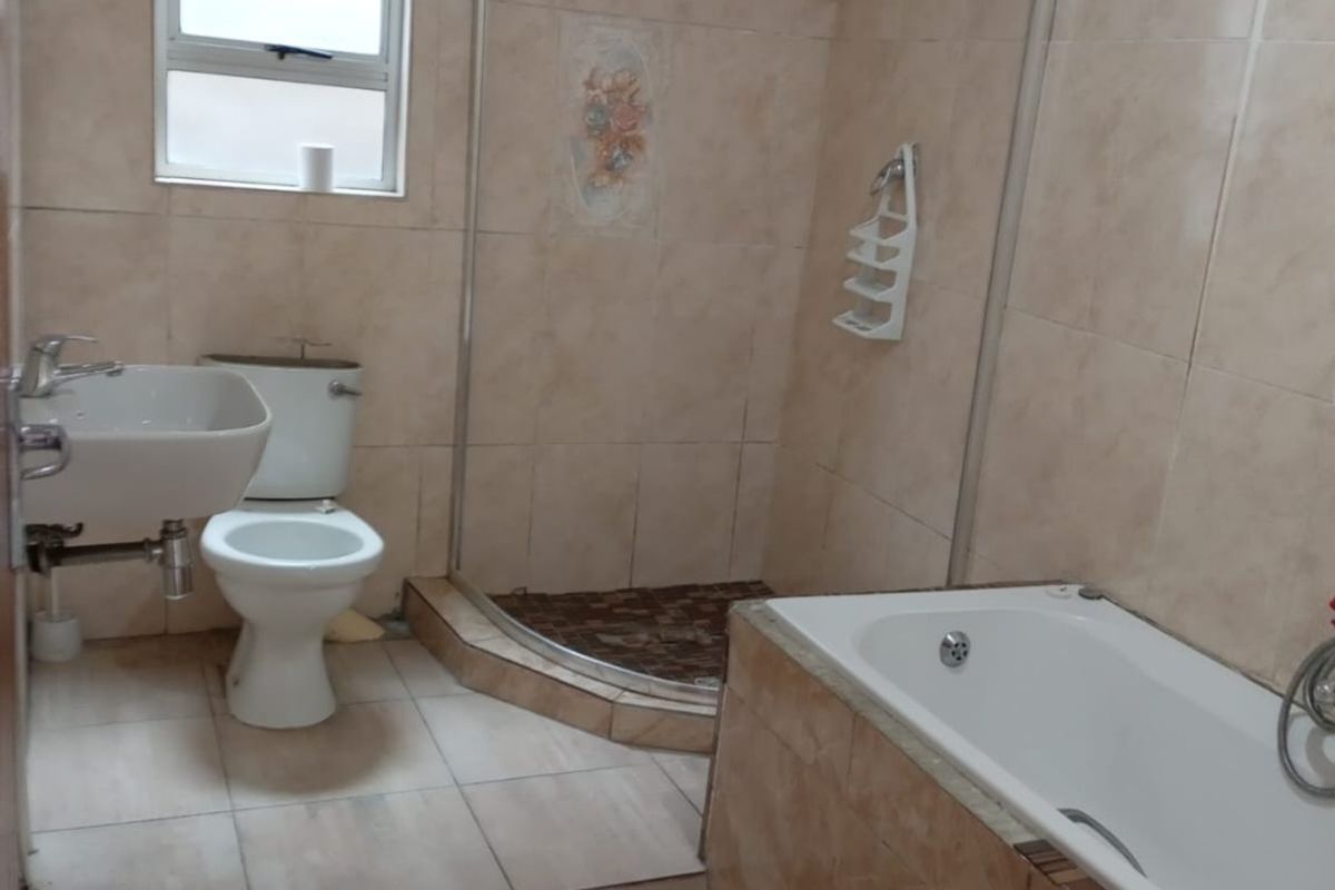 A functional bathroom featuring a separate shower enclosure, bathtub, pedestal basin, and toilet with neutral tiled finishes throughout.