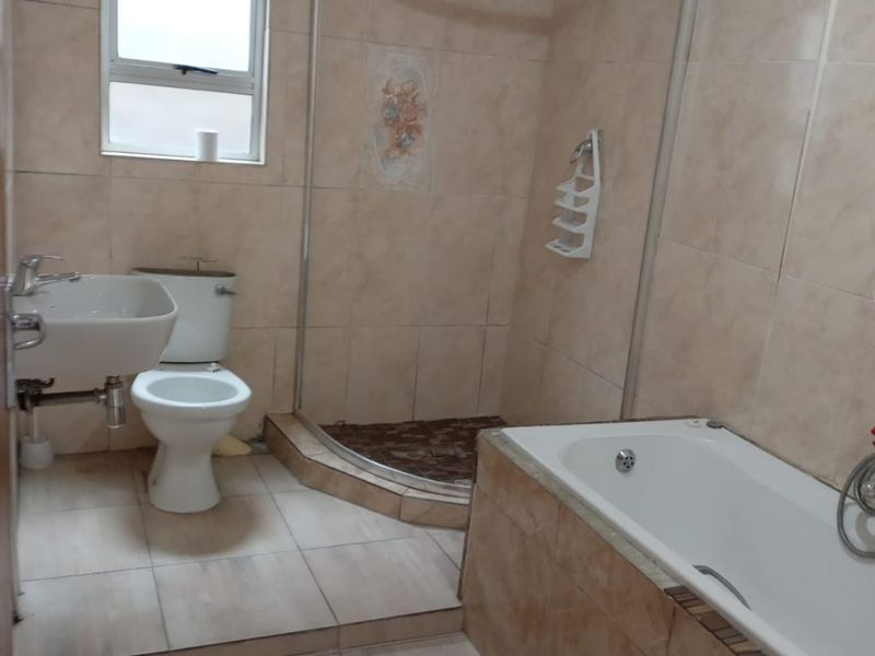 A functional bathroom featuring a separate shower enclosure, bathtub, pedestal basin, and toilet with neutral tiled finishes throughout.
