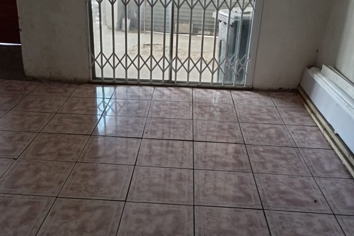 An empty living area featuring ceramic floor tiles and a security gate leading to the exterior.