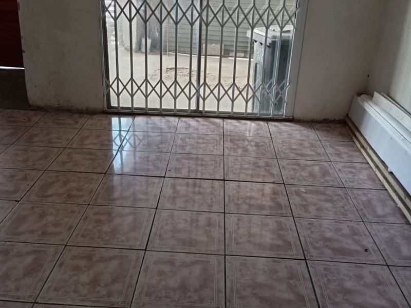 An empty living area featuring ceramic floor tiles and a security gate leading to the exterior.