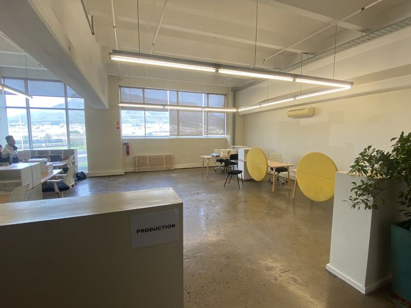 Open-plan commercial office space featuring polished concrete floors, exposed ceilings, large windows with natural light, and integrated air conditioning.