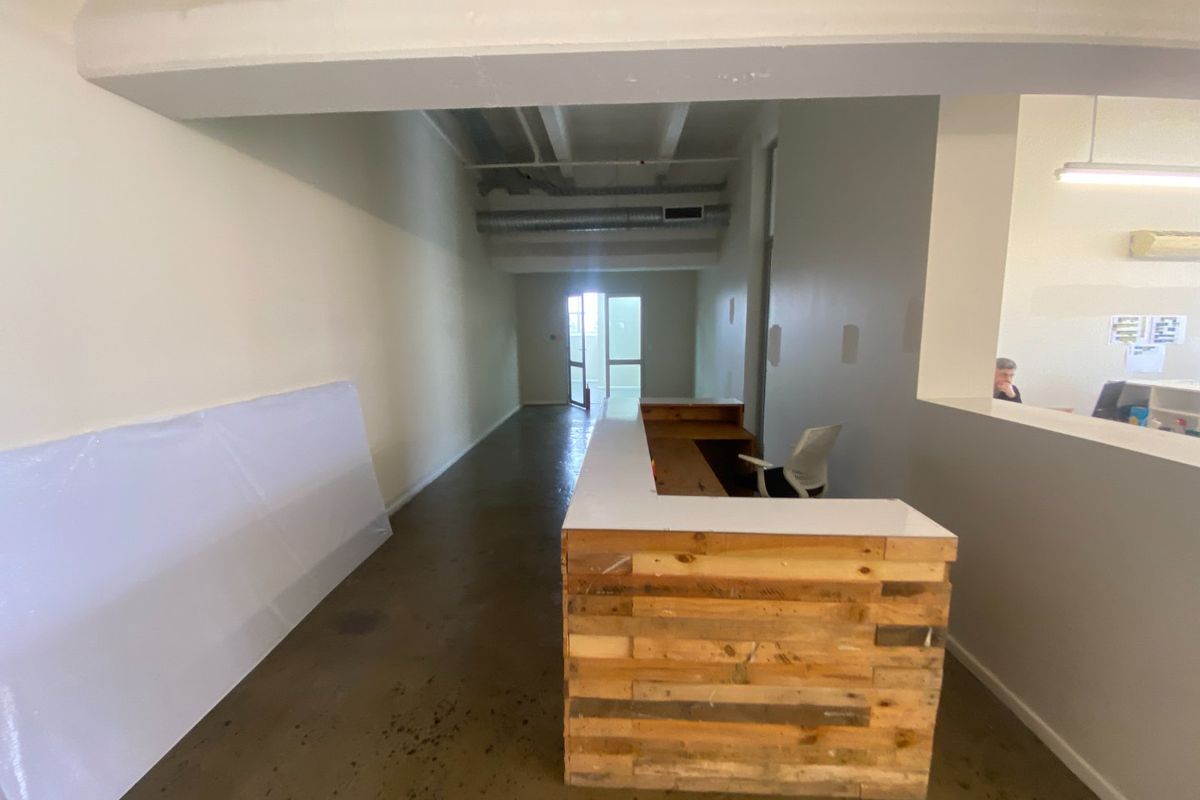 Commercial entry area featuring a custom wood-paneled reception desk, exposed industrial ceiling ductwork, and polished concrete flooring.