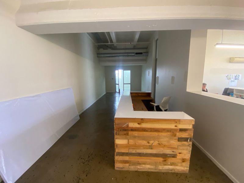 Commercial entry area featuring a custom wood-paneled reception desk, exposed industrial ceiling ductwork, and polished concrete flooring.