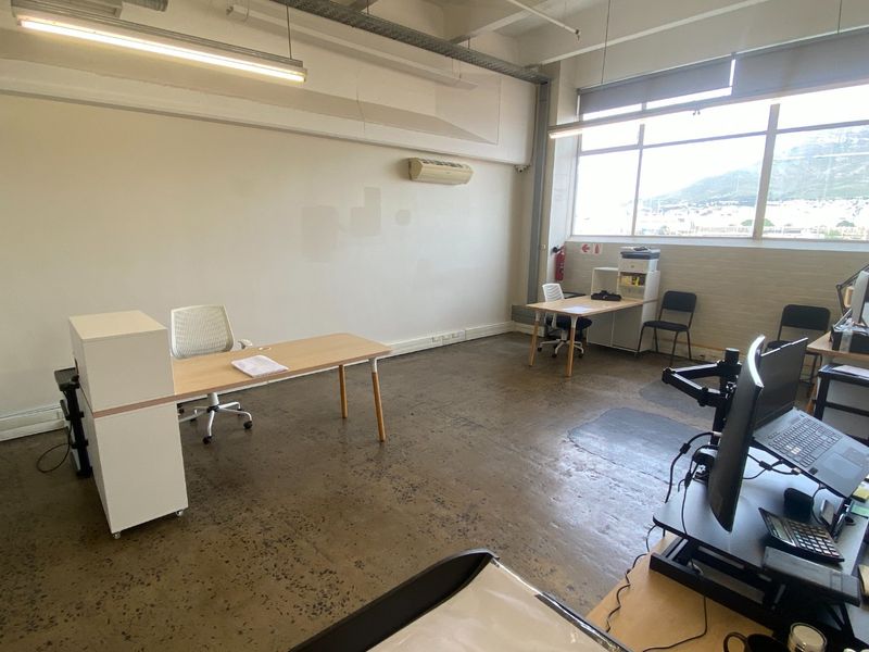 Open-plan commercial office space featuring polished concrete floors, exposed ceiling services, and large windows providing natural light and mountain views.
