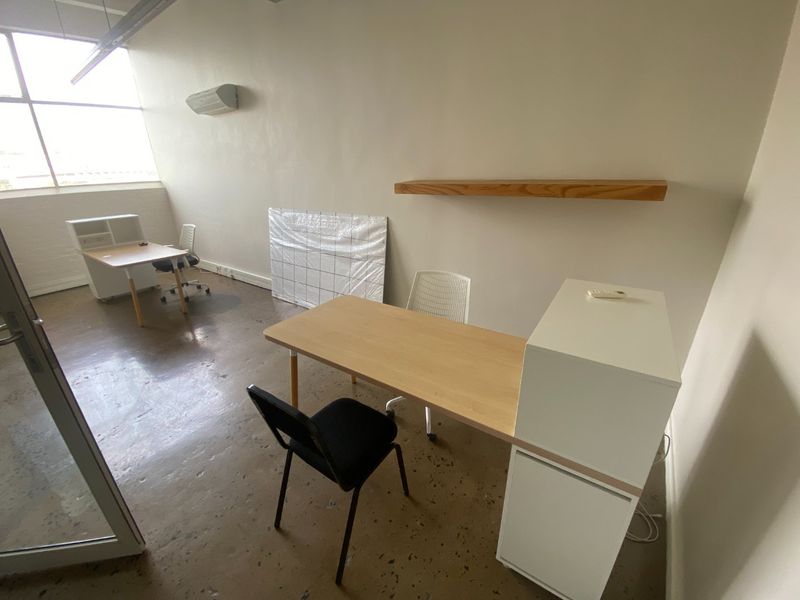 A functional commercial office space featuring industrial concrete flooring, a split-system air conditioner, and a large window providing natural light.