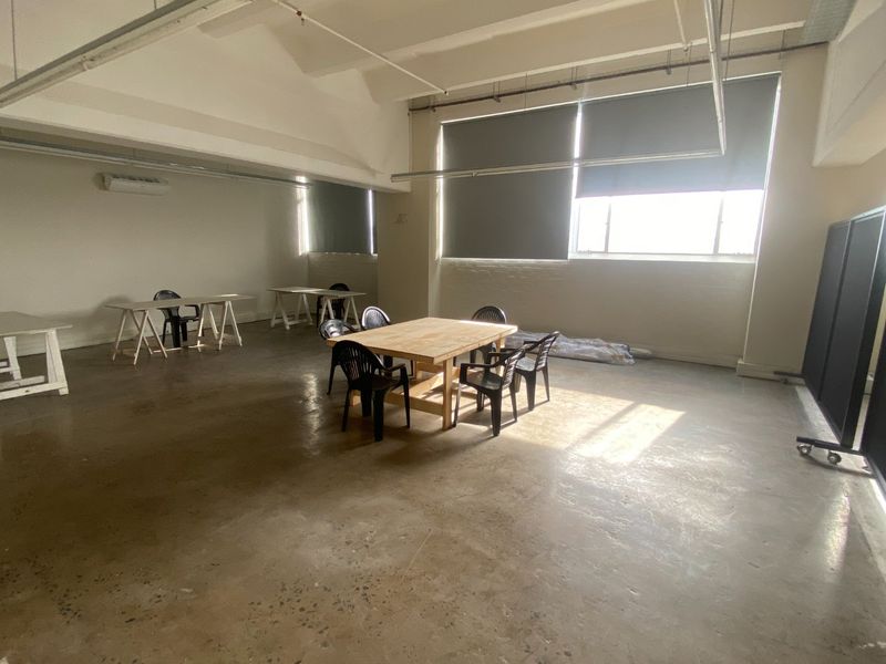 Spacious commercial office area featuring polished concrete floors, exposed ceiling beams, and large windows with roller blinds, offering a versatile open-plan workspace.