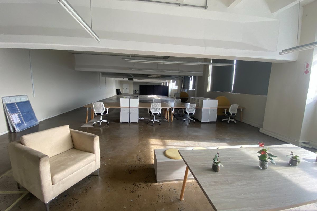 Spacious open-plan commercial office area featuring polished concrete floors, exposed ceiling beams, and large windows providing ample natural light.