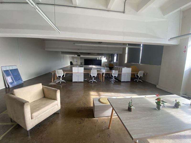 Spacious open-plan commercial office area featuring polished concrete floors, exposed ceiling beams, and large windows providing ample natural light.