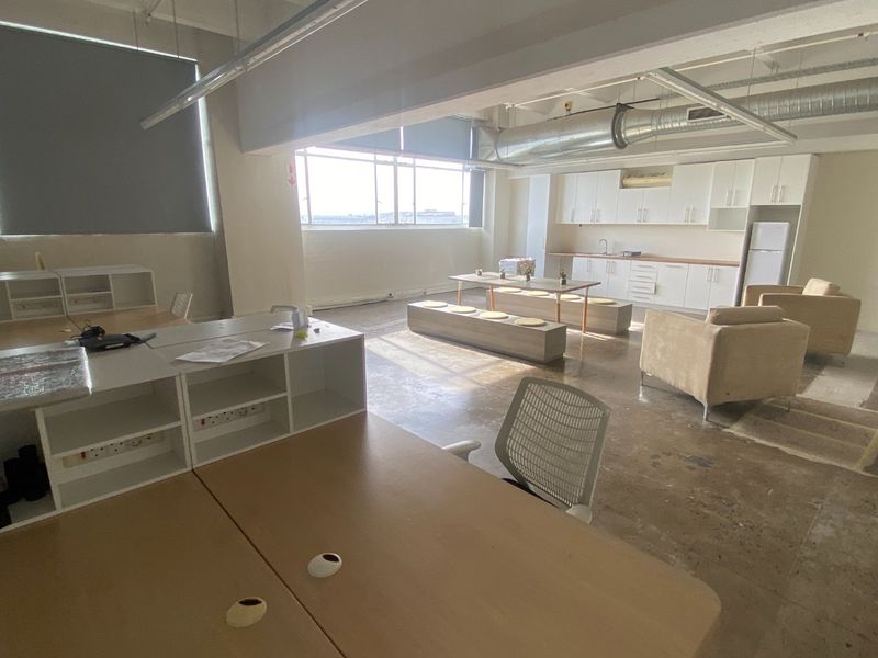 Spacious open-plan commercial office area featuring polished concrete floors, exposed industrial ducting, and a functional kitchenette with white cabinetry.