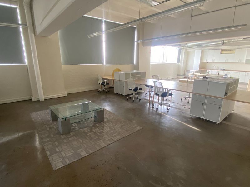 Spacious open-plan commercial office area featuring polished concrete floors, exposed ceiling beams, and an integrated kitchenette with ample natural light.