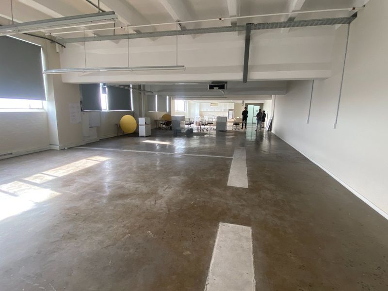 Spacious open-plan commercial office area featuring polished concrete floors, exposed industrial ceilings, and large windows with roller blinds.