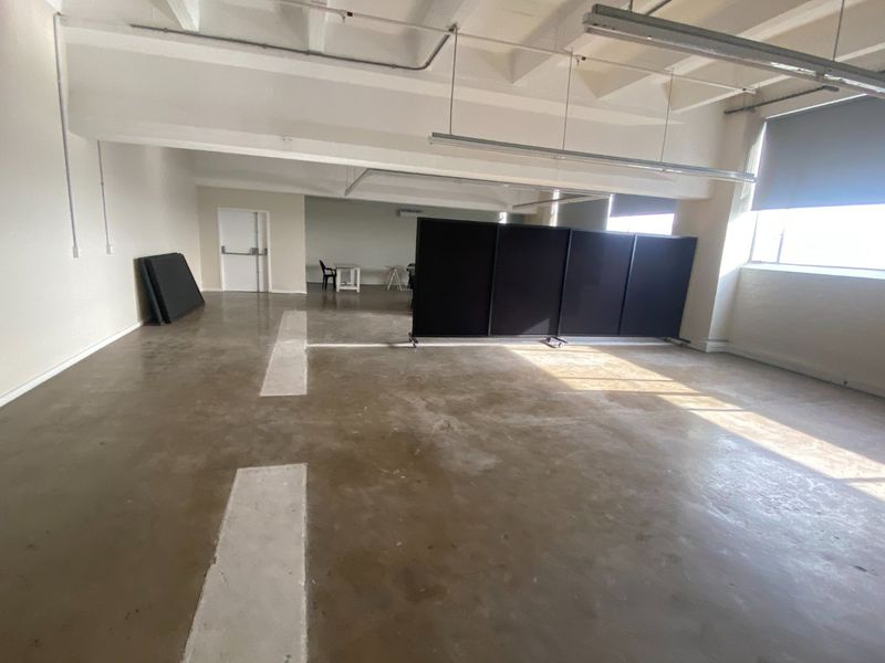 Spacious open-plan commercial office area featuring industrial-style exposed ceilings, polished concrete floors, and large windows providing ample natural light.