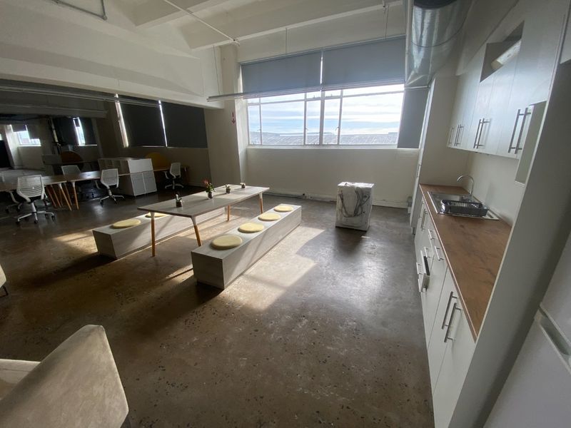 Spacious open-plan commercial office area featuring polished concrete floors, exposed industrial ceiling elements, and a functional kitchenette with modern cabinetry.