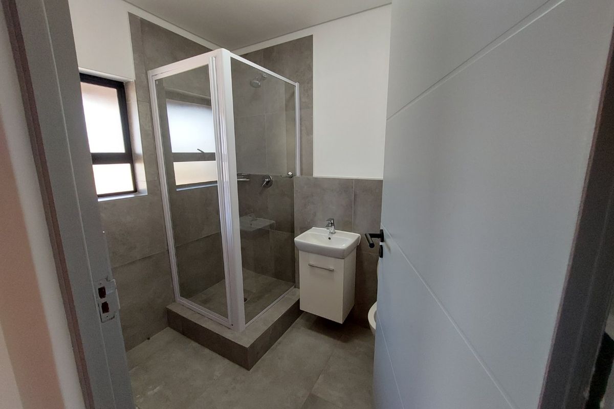 A modern, clean bathroom featuring a glass shower enclosure, wall-mounted vanity with basin, and neutral grey floor-to-ceiling tiling.