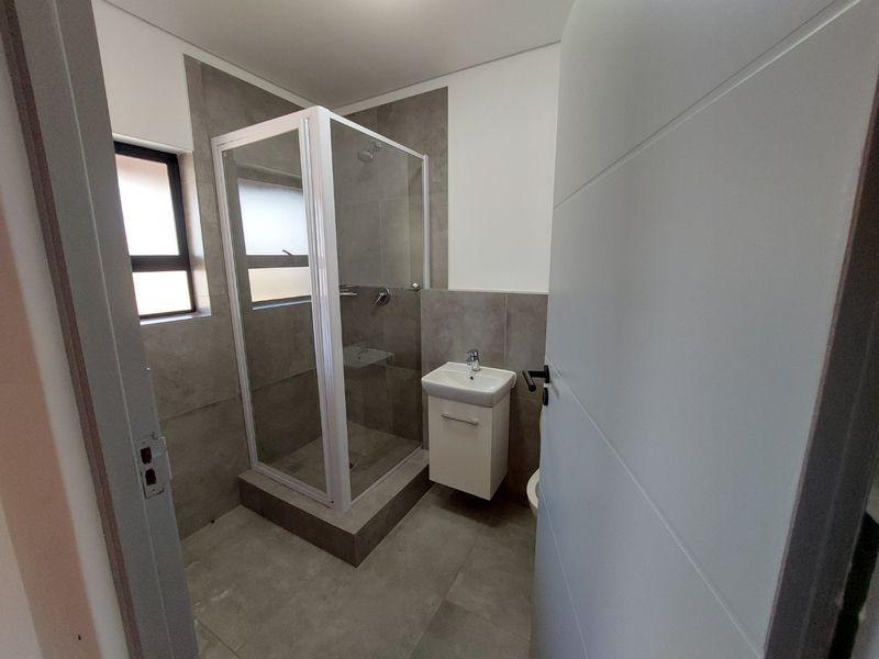 A modern, clean bathroom featuring a glass shower enclosure, wall-mounted vanity with basin, and neutral grey floor-to-ceiling tiling.