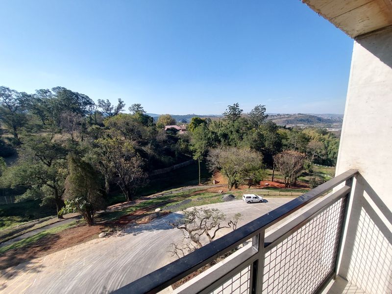 A balcony with a metal balustrade offering an elevated view of the surrounding landscape and parking area.