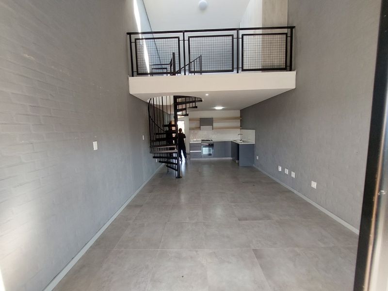 Modern open-plan living area featuring a mezzanine level, spiral staircase, and a sleek kitchen with built-in appliances and contemporary finishes.