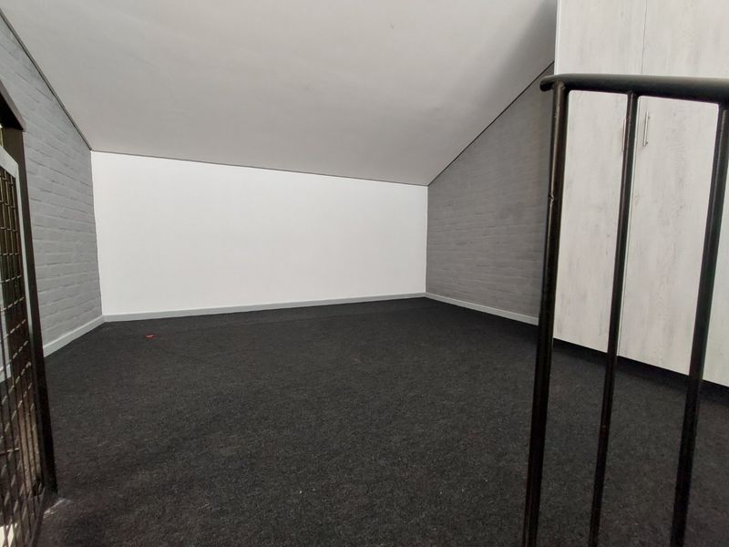 An empty loft-style bedroom featuring sloped ceilings, painted brick walls, and built-in storage cupboards.