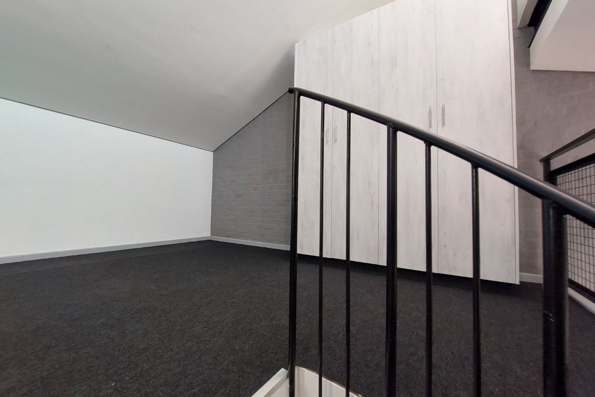 An empty loft-style bedroom featuring built-in cupboards, dark carpeting, and a modern metal staircase railing.
