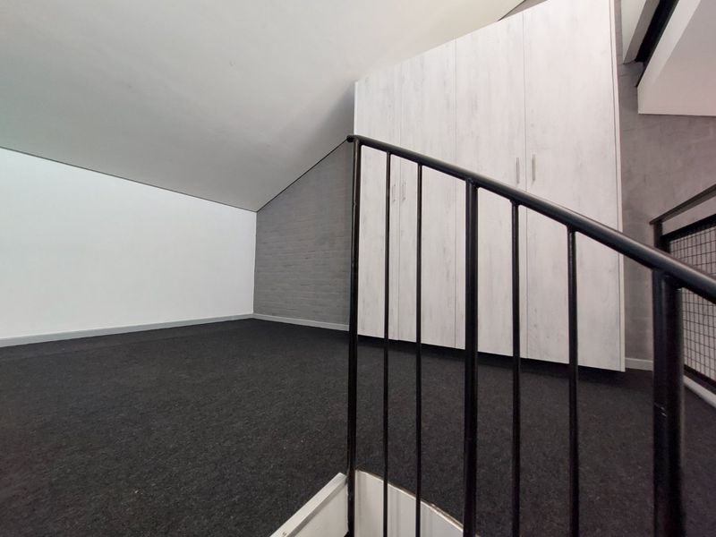 An empty loft-style bedroom featuring built-in cupboards, dark carpeting, and a modern metal staircase railing.