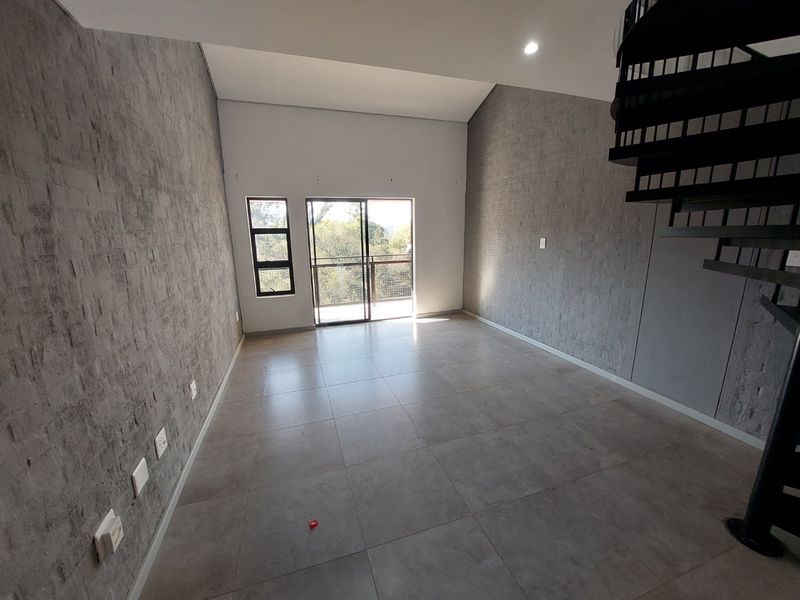 Spacious open-plan living area featuring modern tiled floors, exposed brick walls, a spiral staircase, and access to a balcony through sliding glass doors.