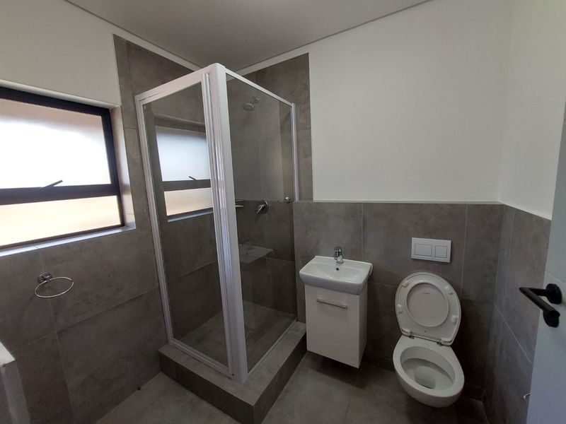 Modern bathroom featuring a glass shower enclosure, wall-mounted vanity with basin, and a wall-hung toilet with neutral grey tiling throughout.