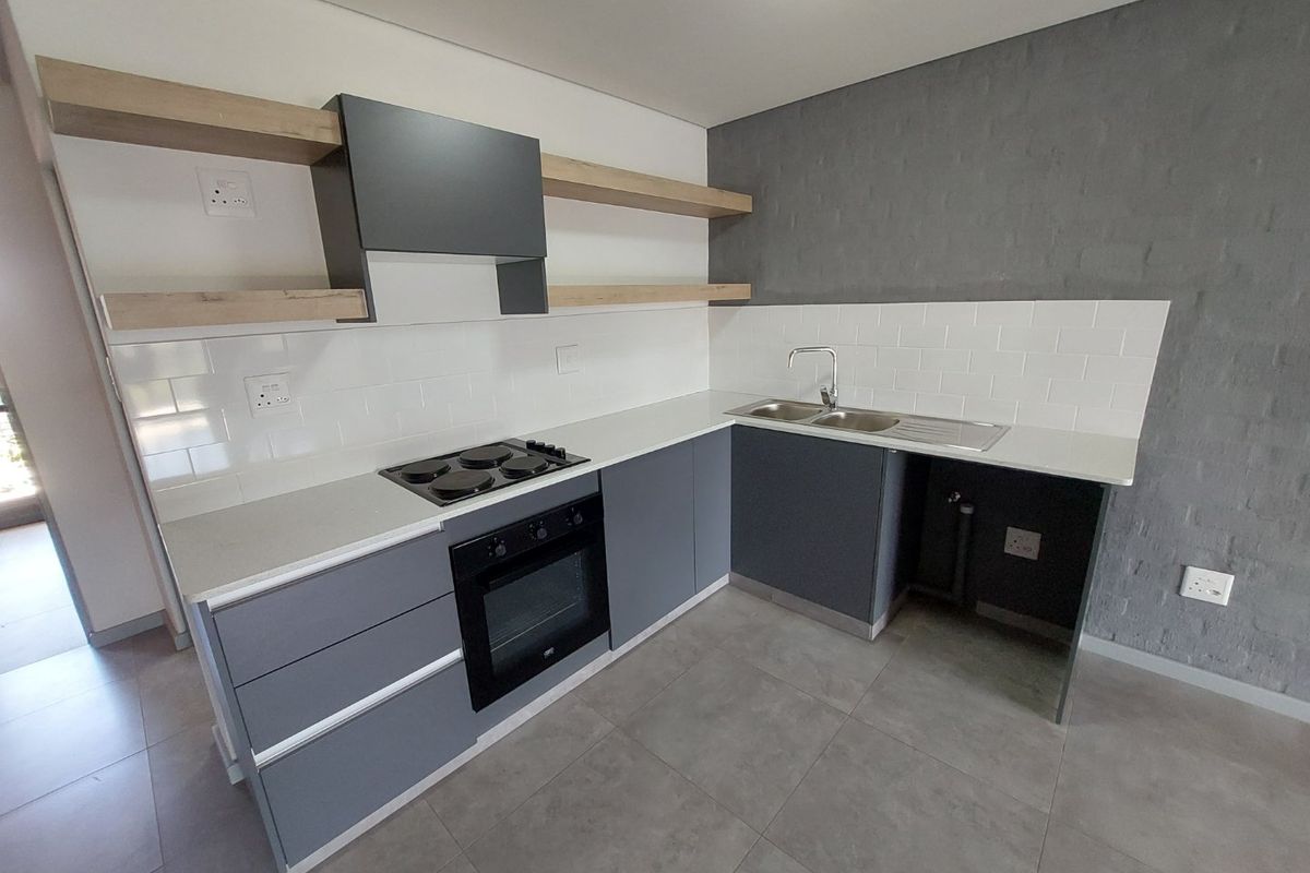 Modern kitchen featuring grey cabinetry, built-in oven, electric hob, extractor fan, double sink, and floating shelves with a stylish tiled splashback.
