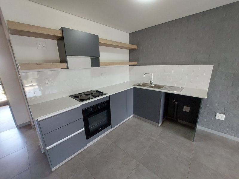 Modern kitchen featuring grey cabinetry, built-in oven, electric hob, extractor fan, double sink, and floating shelves with a stylish tiled splashback.