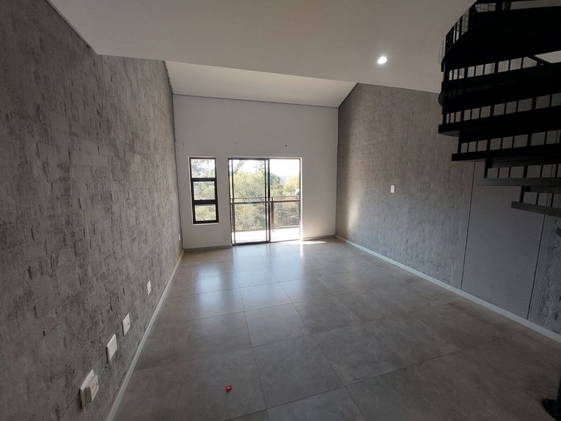 Spacious open-plan living area featuring modern grey tiled floors, textured feature walls, a striking spiral staircase, and access to a private balcony.