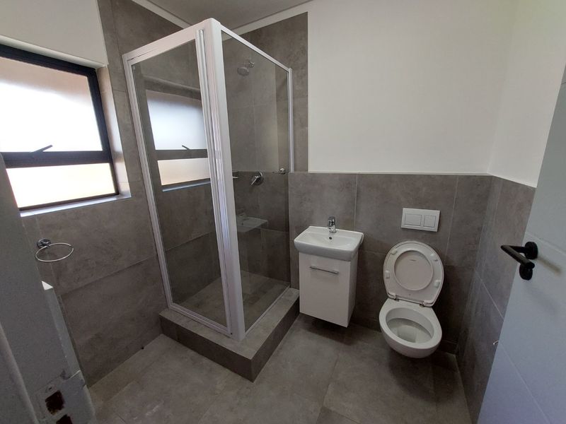 Modern bathroom featuring a glass shower enclosure, wall-mounted toilet, and a vanity basin with neutral grey floor-to-ceiling tiling.